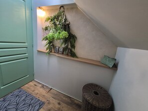 Une pièce avec une étagère en bois, une plante suspendue, un petit tabouret et un tapis à motifs.