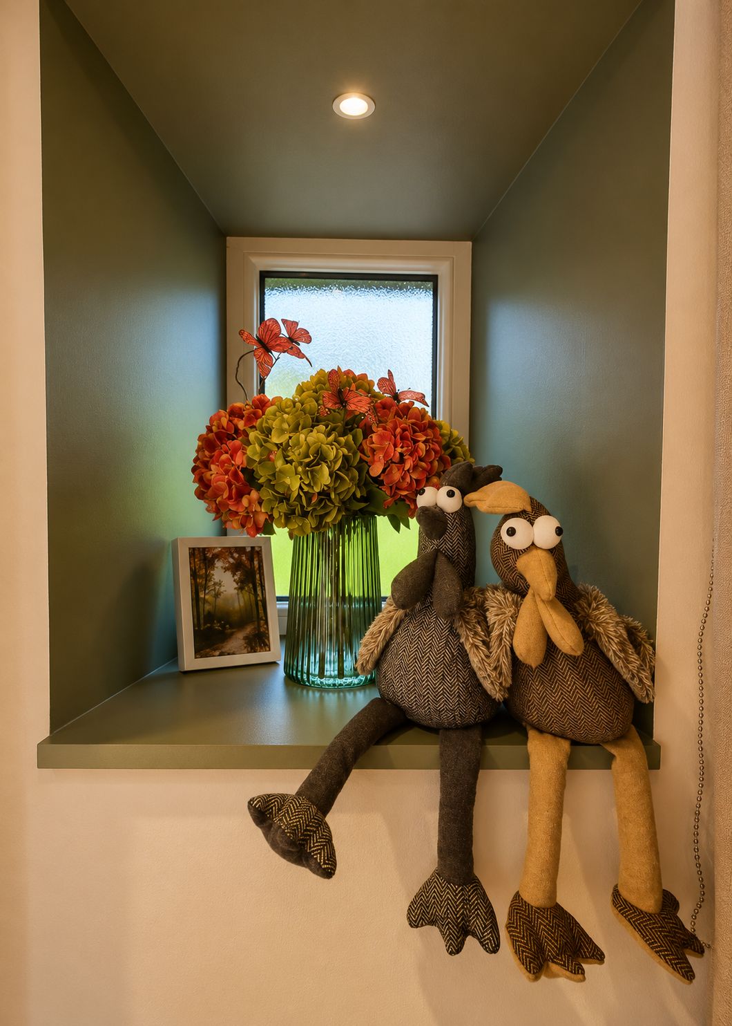 A small room with a window, a vase of flowers, and two plush toys on a shelf.