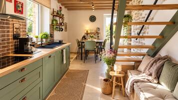 Une cuisine moderne avec un mur de fond en briques, des armoires en bois et un coin repas agrémenté d’un canapé vert et d’une petite table.
