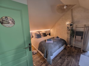Une chambre à coucher avec un lit, une porte verte, un plancher en bois, un ventilateur de plafond et un petit tapis.