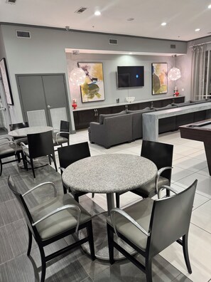 Eine moderne Hotelhalle mit einem runden Esstisch, grauen Stühlen, einer Couch, einem Flachbildfernseher und abstrakter Kunst an der Wand.