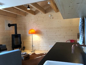 Ein Holzinnenraum mit Kamin, Stehlampe, einer Couch und einer Küchenzeile.