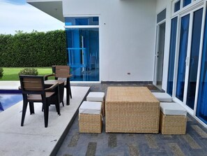 An outdoor patio with wicker furniture, a pool, and a modern building with large windows. - Serene Seaside Retreat in Juan de Acosta - Private Pool & Comfort (Juan de Acosta)
