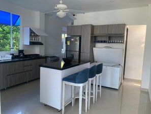 Een moderne keuken met een centraal eiland, barstoelen, een plafondventilator en een koelkast.