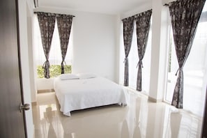 Quarto com cama, cortinas e vista para o verde lá fora.
