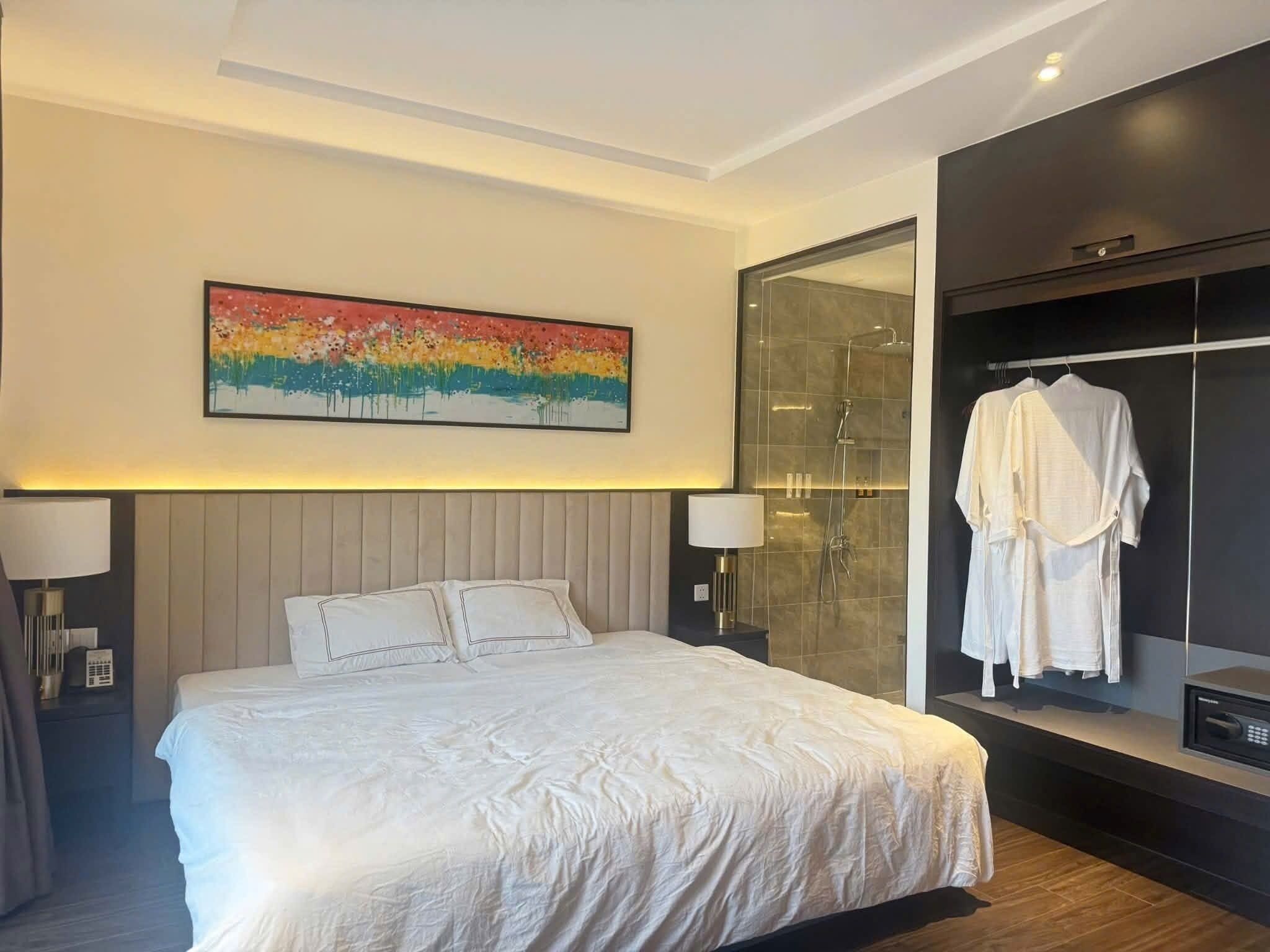 Ett modernt hotellrum med en stor säng, en duschkabin med glasväggar och en badrock som hänger på en klädstång.