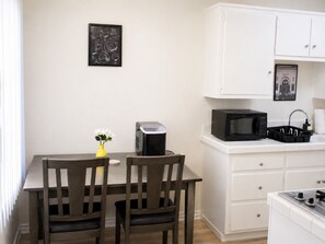 A small kitchenette with a microwave, toaster, and sink. There is a framed picture on the wall and a vase with flowers on the table. - Hidden NoHo Nook (Los Angeles)