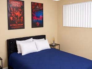 A bedroom with a bed, two posters, a lava lamp, and a window with blinds. - Hidden NoHo Nook (Los Angeles)