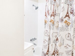 A bathroom with a shower curtain featuring Parisian motifs, a white tiled wall, and a bathtub. - Hidden NoHo Nook (Los Angeles)