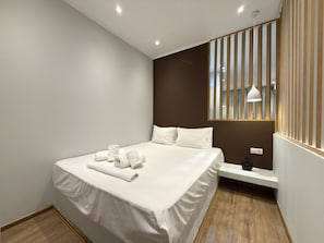 Een moderne hotelkamer met een net opgemaakt bed, een nachtkastje en een raam met verticale jaloezieën.