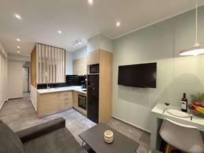 A modern kitchen with a built-in oven, a black refrigerator, and a flat-screen TV mounted on the wall. - SmartLiving Central Apt 10 (Thessaloniki)