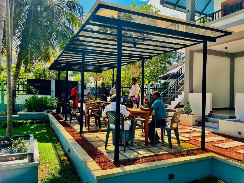 An outdoor seating area with tables and chairs, surrounded by a garden with palm trees and a pool.