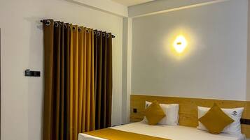 A hotel room with a bed, a ceiling fan, a wall-mounted light, and a window with curtains.