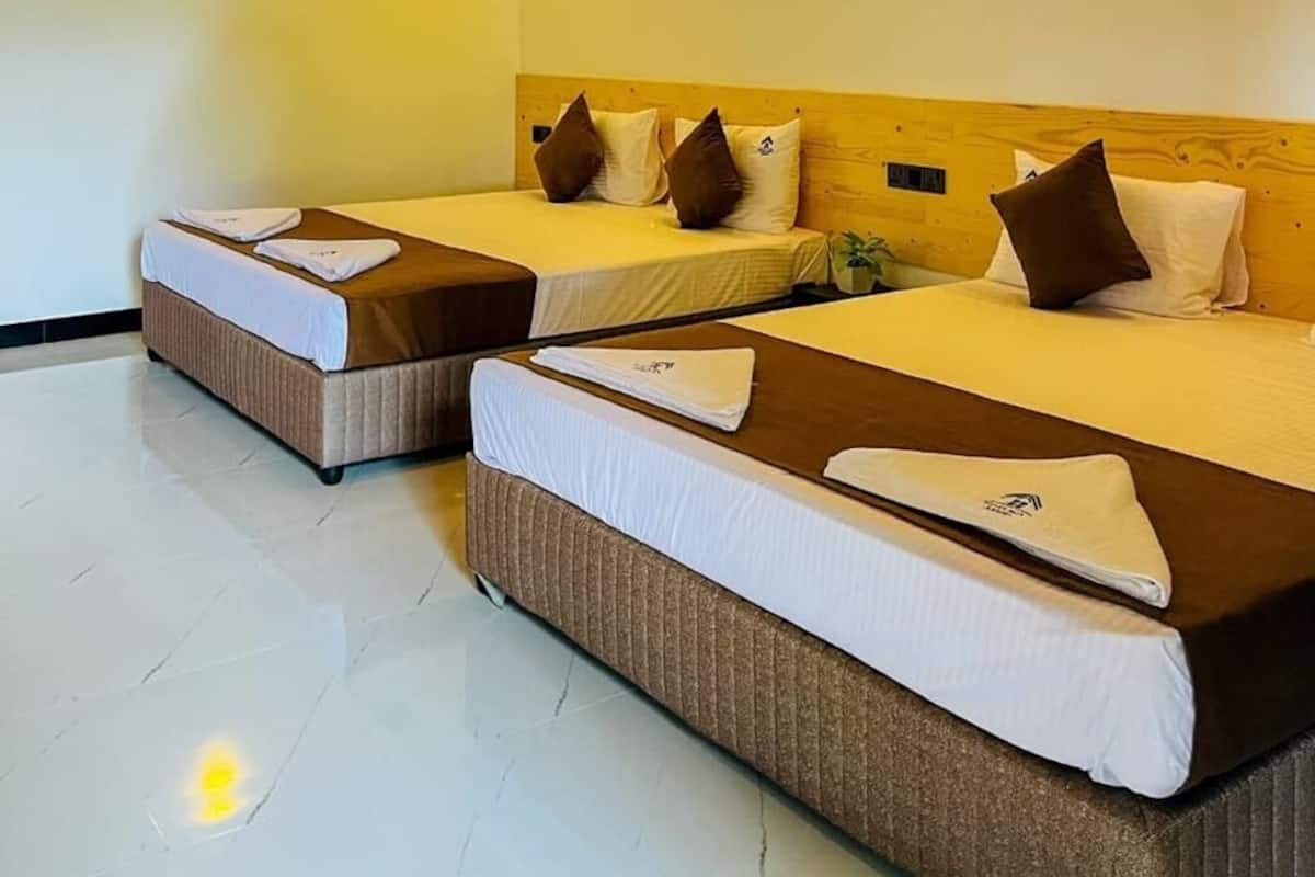A hotel room with two beds, wooden ceiling, and wall-mounted lights.