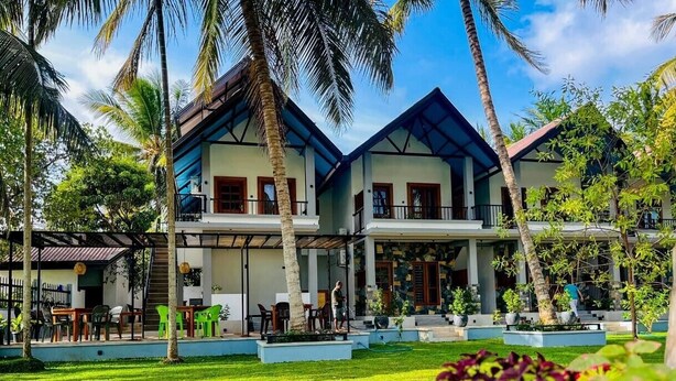 A two-story building with a covered patio area, surrounded by palm trees and greenery. - Silver Palm Resort (Anuradhapura)