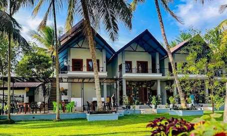 A two-story building with a covered patio area, surrounded by palm trees and greenery.. Silver Palm Resort