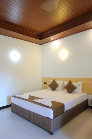 Una habitación de hotel con techo de madera, una cama grande con ropa blanca y almohadas marrones, y dos lámparas fijadas a la pared.