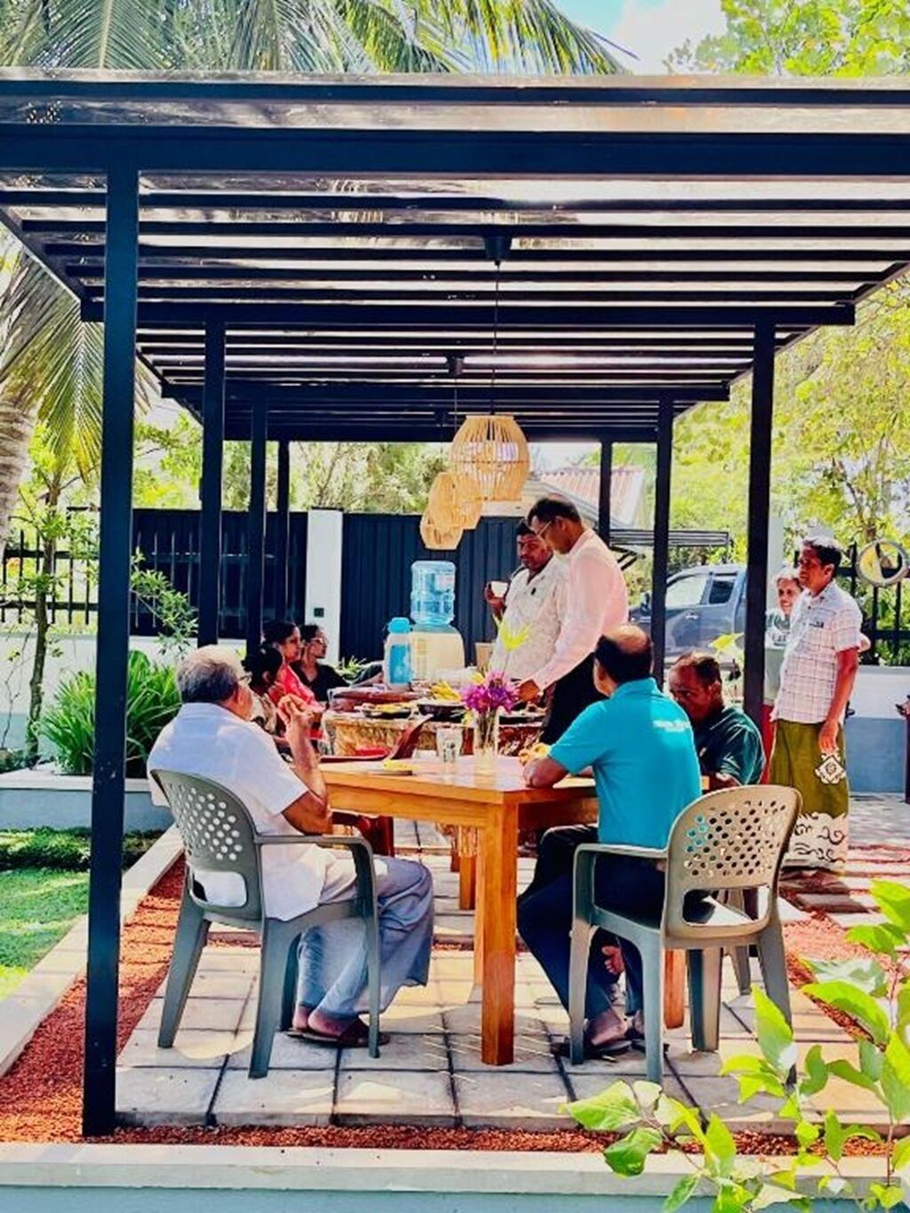 Un espace extérieur abrité, aménagé pour prendre les repas, avec une table et des chaises, entouré de verdure et sous un ciel dégagé.