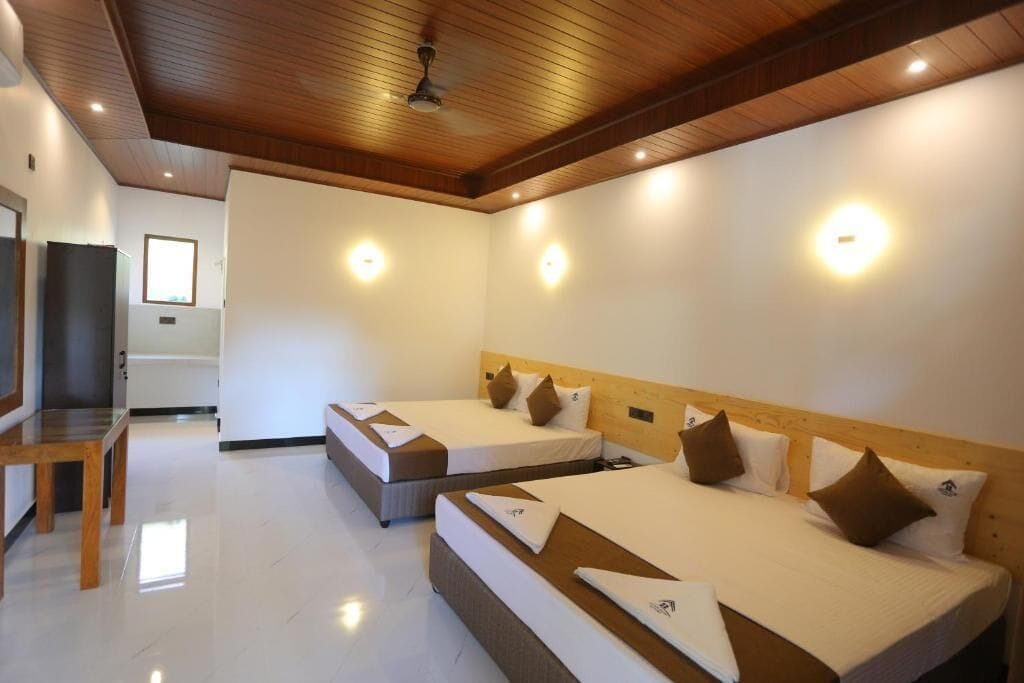 A hotel room with three beds, wooden ceiling, and wall-mounted lights.