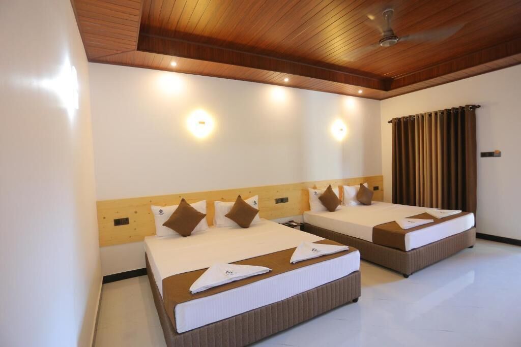 A hotel room with two beds, wooden headboards, ceiling fans, and wall-mounted lights.