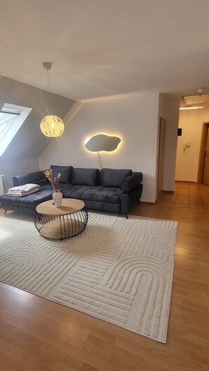 Ein modernes Wohnzimmer mit einem dunkelblauen Sofa, einem runden Couchtisch, einem weiĂen Teppich und einer Pendelleuchte.