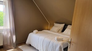 Makuuhuoneessa on puulattia, valkoisilla lakanoiden peitetty sänky, läpikuultavilla verhoilla varustettu ikkuna ja kattovalaisin.