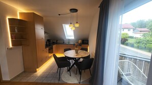 Moderni keittiö, jossa on puiset kaapit, ruokailutila pyöreällä pöydällä ja tuoleilla sekä parveke, jossa on valkoinen tuoli.