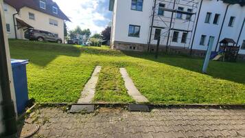 A paved pathway leading uphill with a grassy area, a parked car, and a building with multiple windows and scaffolding.
