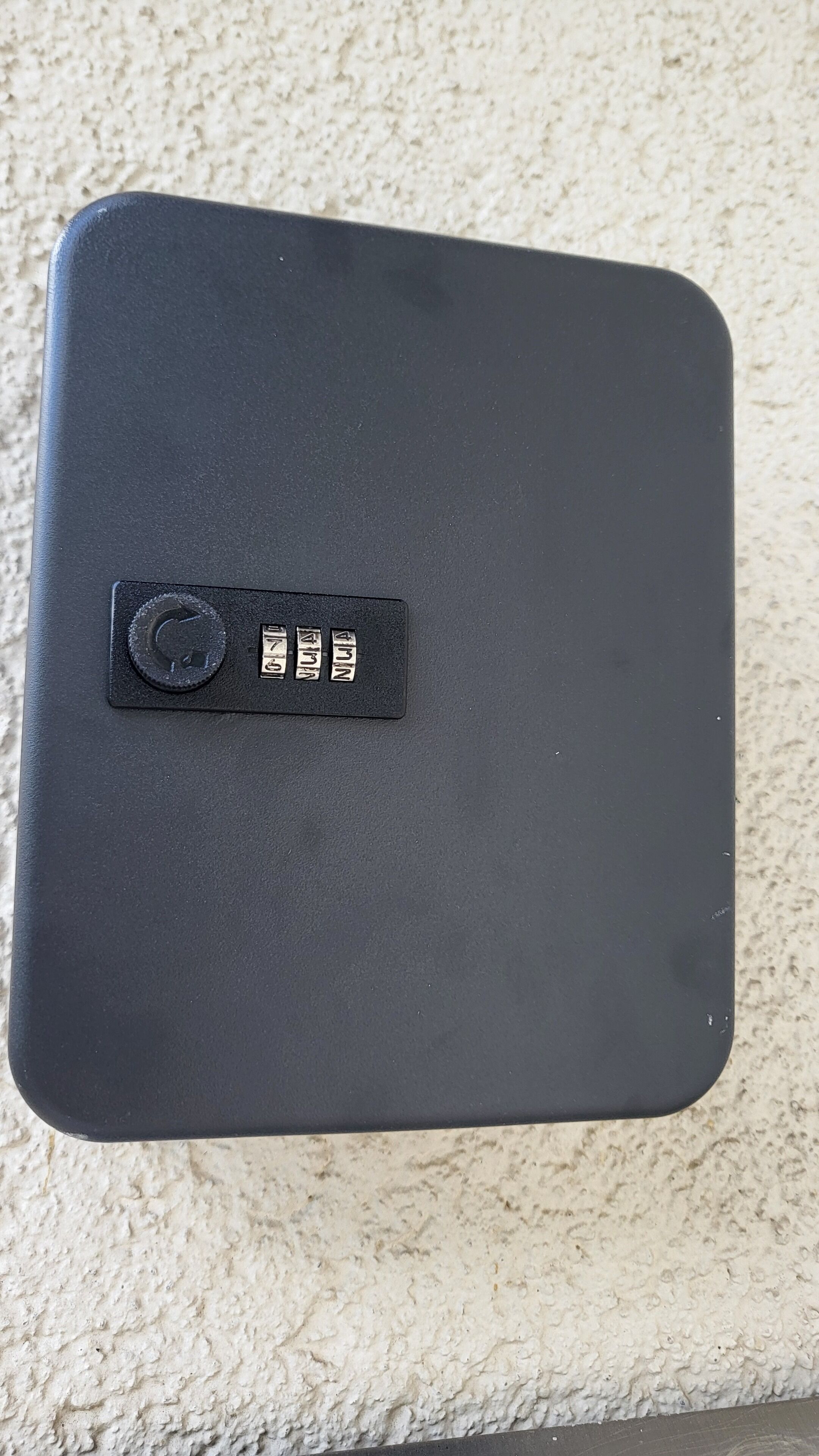 Un objeto rectangular negro con un botón circular y tres etiquetas metálicas con números.