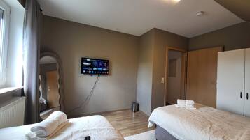 A hotel room with two beds, a TV mounted on the wall, a mirror, and a wardrobe.