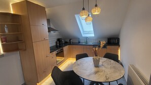 Kompakti keittiö, jossa on puiset kaapit, pyöreä marmoripöytä ja riippuvalaisimet.