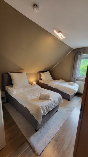 Et moderne soveværelse med to senge, en loftlampe og et vindue med gardiner.