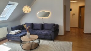 En moderne stue med en mørkeblå sofa, et rundt træbord og en dekorativ vase med tørrede blomster.