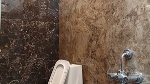 Et badeværelse med toilet, brusearmatur på væggen og en marmorvæg.