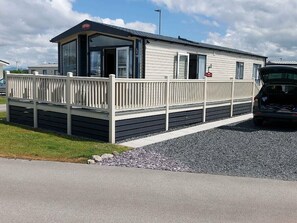 A mobile home with a fenced deck, a carport, and a gravel driveway. - Ocean Edge Leisure Park - Holiday Accommodation 1317 (Morecambe)