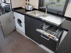 A compact kitchen with a washing machine, a dishwasher, a sink, and a toaster. - Ocean Edge Leisure Park - Holiday Accommodation 1317 (Morecambe)