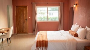 A bedroom with a bed, a desk, and a window with curtains. - Résidence L'Eau Vive (Cotonou)