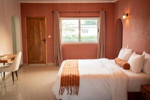Ein Schlafzimmer mit Bett, Schreibtisch und einem fensterbepflanzten Fenster.
