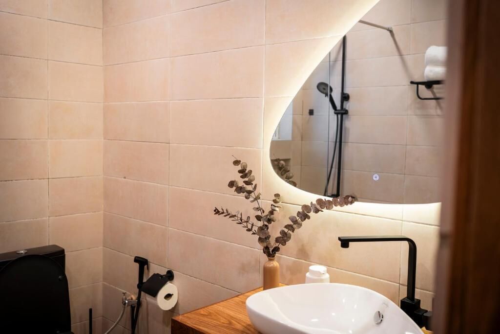 A bathroom with a white sink, a mirror, a toilet, and a shower area.