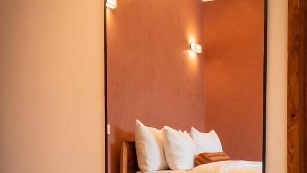 A hotel room with a bed, a wooden nightstand, and a mirror reflecting the room. - Résidence L'Eau Vive (Cotonou)