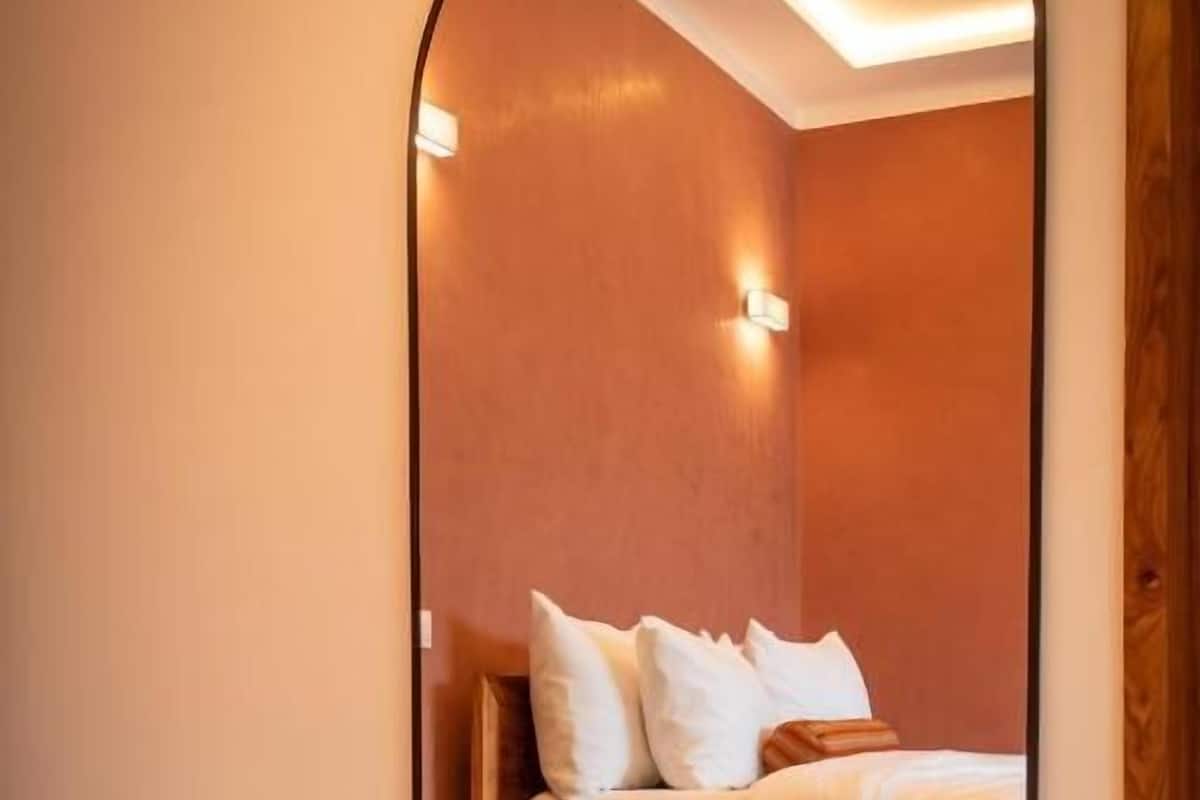 Habitación de hotel con cama, mesita de noche de madera y un espejo que refleja la habitación.