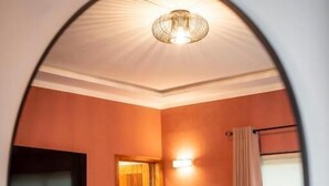 A bedroom with a bed, a desk, a chair, a television, and a door. - Résidence L'Eau Vive (Cotonou)