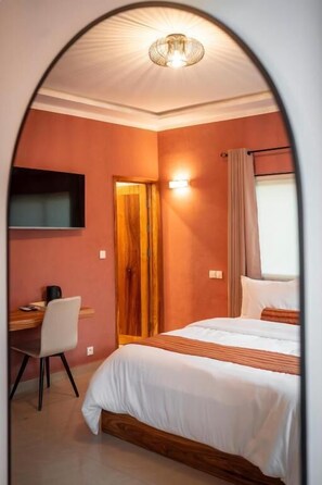 Ein Schlafzimmer mit einem Bett, einem Schreibtisch, einem Stuhl, einem Fernseher und einer Tür.