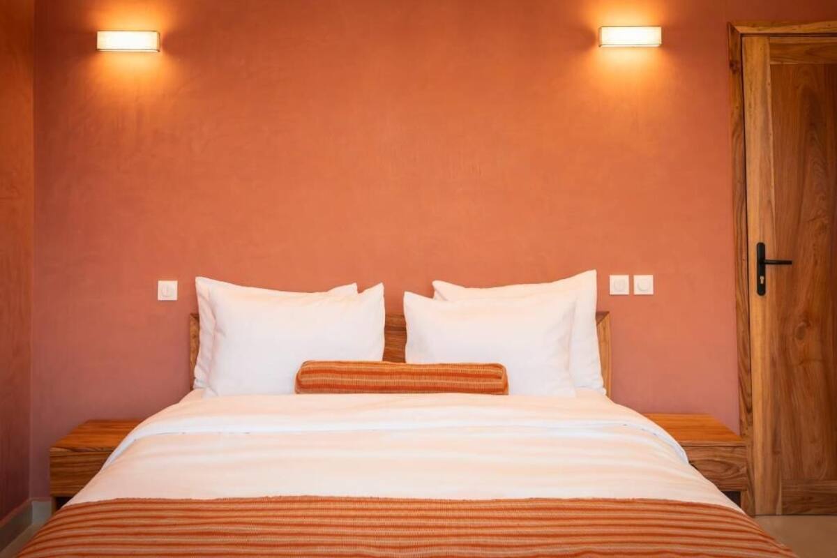 Una habitación de hotel con cama, dos mesitas de noche, una puerta de madera y luces fijadas a la pared.