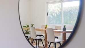 A dining area with a wooden table and chairs, potted plants, and a large window. - Résidence L'Eau Vive (Cotonou)