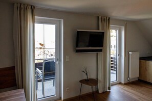 Ein Zimmer mit einer Schiebeglastür, einem an der Wand befestigten Flachbildfernseher, einem kleinen Tisch mit einer Vase und einem Heizkörper.