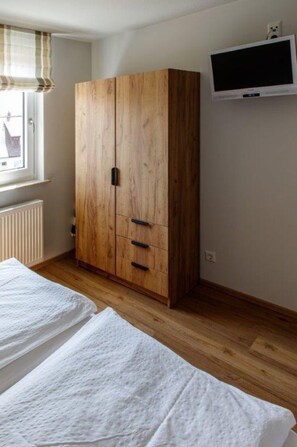 Ein Schlafzimmer mit einem Holzschrank, einem Bett mit weißer Bettwäsche und einem an der Wand montierten Fernseher.