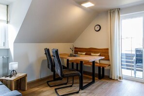Ein gemütlicher Raum mit einem Holztisch, zwei Stühlen, einer Bank, einer Uhr und einem fenster mit Vorhängen.