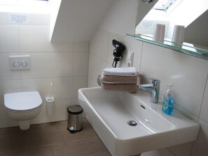 Un bagno moderno con toilette, bidet, cestino, lavandino e asciugacapelli su uno scaffale.
