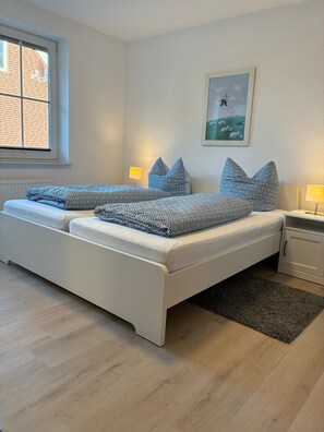 Ein modernes Schlafzimmer mit einem Doppelbett, Nachttischlampen, einem grauen Teppich, einem Fenster mit Blick auf ein Backsteingebäude und einem gerahmten Bild an der Wand.